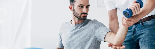 Prise de vue panoramique du physiothérapeute aidant patient avec haltère pendant la récupération — Photo de stock