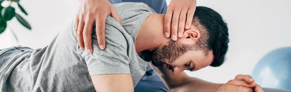 Tiro panorâmico de quiroprático massageando pescoço de homem deitado — Fotografia de Stock