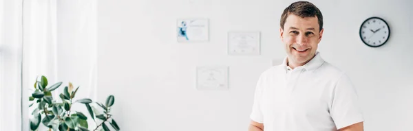 Панорамний знімок усміхненого хіропрактика в лікарні, дивлячись на камеру — стокове фото
