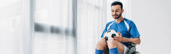Panoramic shot of man in football uniform sitting in Wheelchair and holding soccer ball — Stock Photo