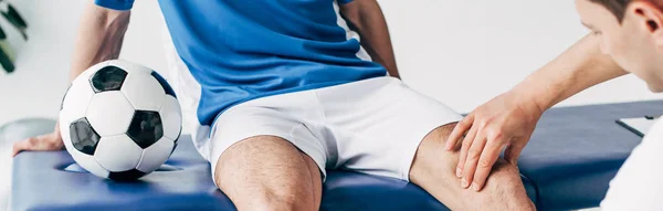 Panoramic shot of Physiotherapist massaging leg of football player in hospital — Stock Photo