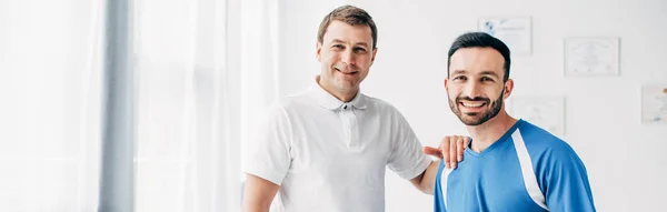 Panoramic shot of smiling Physiotherapist and patient looking at camera in hospital — Stock Photo