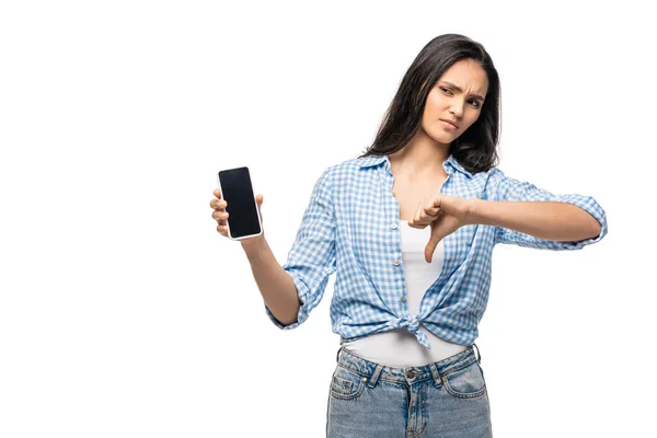 Chica decepcionada sosteniendo teléfono inteligente con pantalla en blanco y mostrando el pulgar hacia abajo aislado en blanco - foto de stock