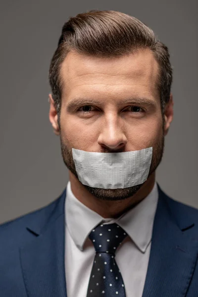 Handsome businessman in suit with duct tape on mouth isolated on grey — Stock Photo