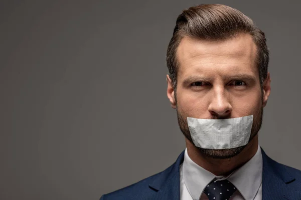 Homem de negócios bonito em terno com fita adesiva na boca em cinza com espaço de cópia — Fotografia de Stock
