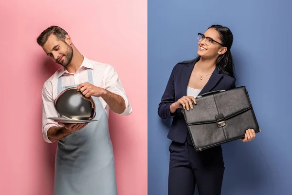 Hombre de delantal con bandeja de servir y mujer de negocios sonriente con maletín en azul y rosa - foto de stock