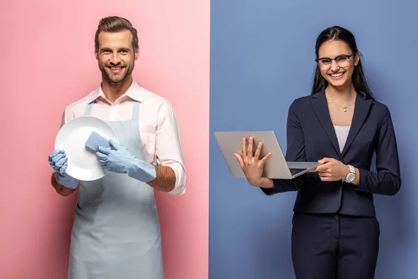 Uomo in grembiule piatto di lavaggio mentre donna d'affari utilizzando il computer portatile su blu e rosa — Foto stock