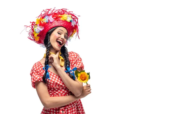 Excitada chica en ropa festiva y sombrero de paja tocando la barbilla aislado en blanco - foto de stock