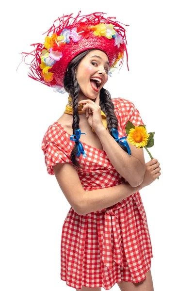 Excitada chica en ropa festiva y sombrero de paja tocando la barbilla aislado en blanco - foto de stock