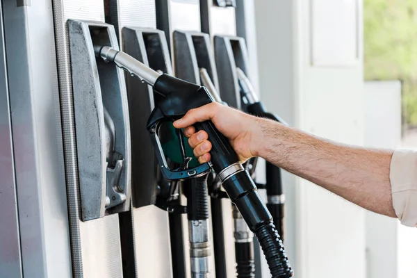 Vista recortada del hombre sosteniendo la boquilla de combustible en la gasolinera - foto de stock