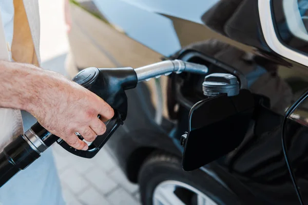Mann hält Zapfsäule und tankt schwarzes Auto an Tankstelle — Stockfoto