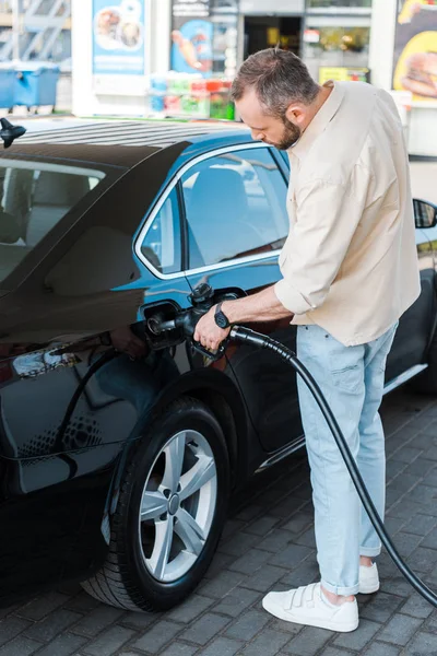 Uomo barbuto rifornimento auto nera mentre in piedi al distributore di benzina — Foto stock