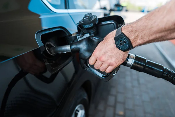 Vista recortada del hombre sosteniendo la bomba de combustible y repostaje de automóviles en la gasolinera - foto de stock