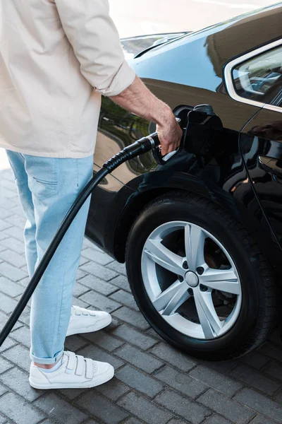 Cropped view of man holding fuel nozzle and refueling automobile at gas station — Stock Photo