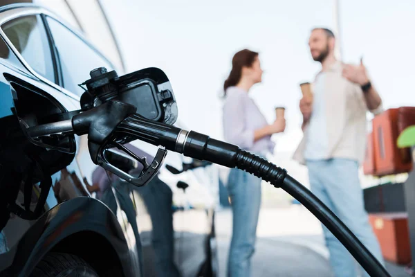 Fuoco selettivo di rifornimento nero dell'automobile con benzine vicino all'uomo e alla donna sulla stazione di servizio — Foto stock