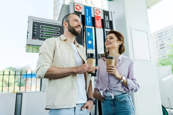 Low angle view of happy man and woman holding paper cups at gas station — Stock Photo