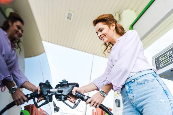 Vue à faible angle de la femme heureuse tenant pompe à carburant tout en ravitaillant la voiture avec benzine — Photo de stock