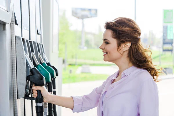 Mulher feliz segurando bomba de combustível enquanto sorrindo no posto de gasolina — Fotografia de Stock
