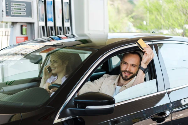 Felice uomo in possesso di carta di credito durante la guida di auto al distributore di benzina — Foto stock