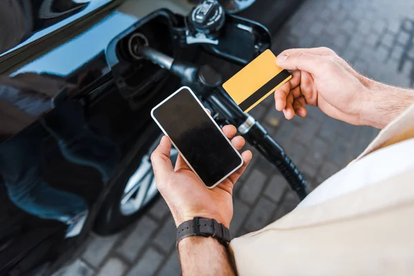 Vista ritagliata di uomo in possesso di carta di credito vicino smartphone con schermo bianco — Foto stock