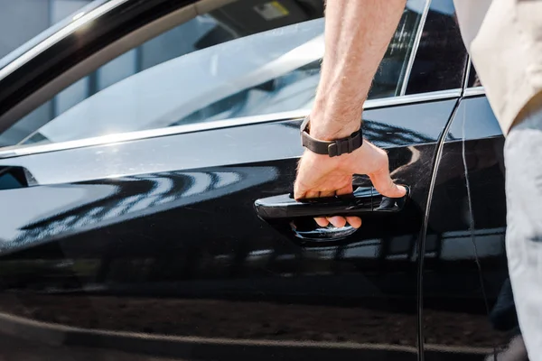 Vista recortada del hombre de pie cerca del coche y tocar el mango al abrir la puerta - foto de stock