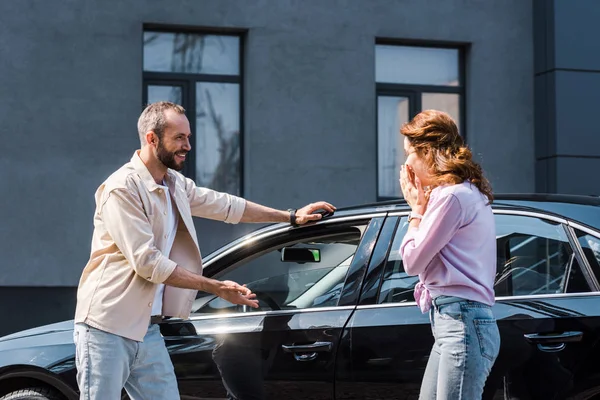 Cheerful man gesturing near modern car and standing near excited woman — Stock Photo