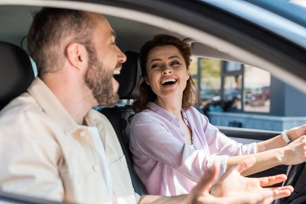 Selective focus of cheerful woman looking at happy man gesturing in car — Stock Photo