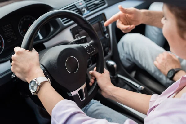 Обрізаний вид чоловіка, який вказує пальцем на кермо біля жінки в машині — стокове фото