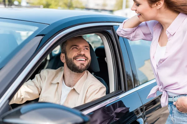 Selektiver Fokus einer glücklichen Frau, die mit der Hand in der Tasche neben einem fröhlichen Mann im Auto steht — Stockfoto