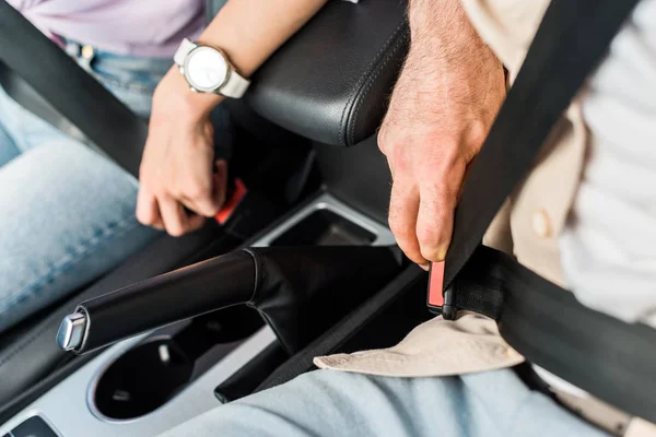 Visão cortada de homem e mulher fixando cintos de segurança enquanto sentado no carro — Fotografia de Stock