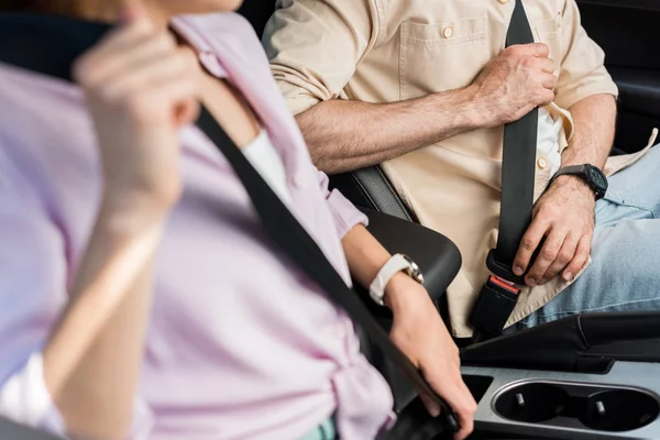 Visão cortada de mulher e homem fixando cintos de segurança enquanto sentado no carro — Fotografia de Stock