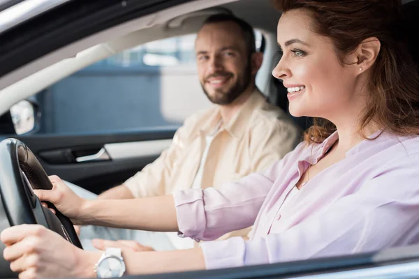 Enfoque selectivo de la mujer feliz conduciendo coche cerca de hombre guapo - foto de stock
