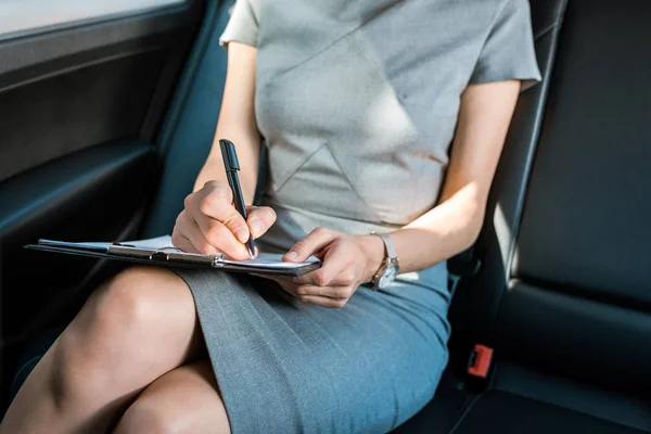 Vue recadrée de la femme assise dans la voiture et l'écriture tout en tenant presse-papiers — Photo de stock