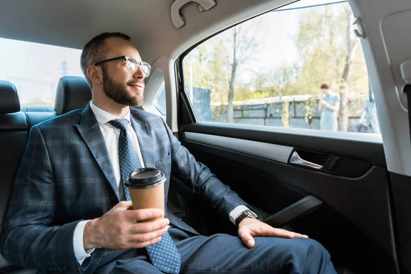 Счастливый бизнесмен держит бумажную чашку и смотрит в окно в машине — стоковое фото