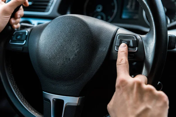 Vista recortada del hombre apuntando con el dedo al botón mientras sostiene el volante - foto de stock