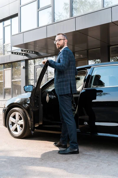 Vista de ángulo bajo del hombre de negocios en traje de pie cerca de coche negro - foto de stock