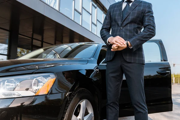 Vista cortada de homem de negócios tocando relógio e de pé perto de carro preto — Fotografia de Stock
