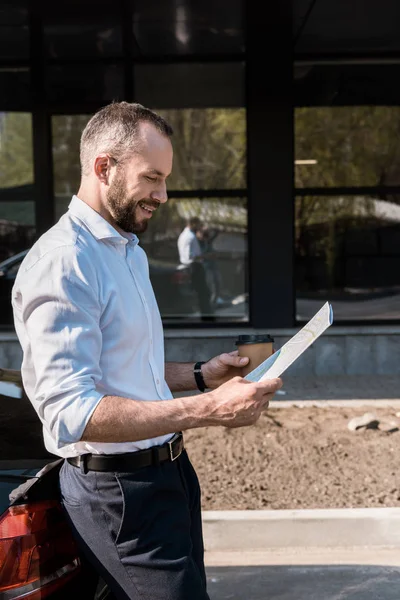 Glücklicher Geschäftsmann schaut auf Landkarte, während er neben schwarzem Auto steht — Stockfoto