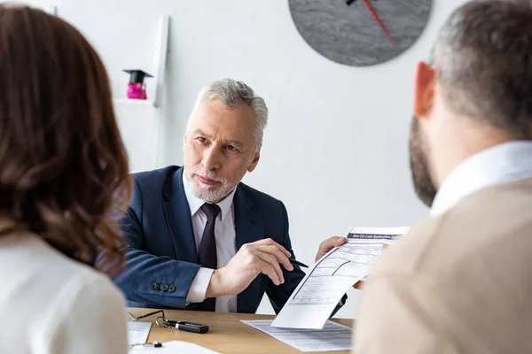 Selective focus of bearded car dealer holding contract and pen near customers — Stock Photo