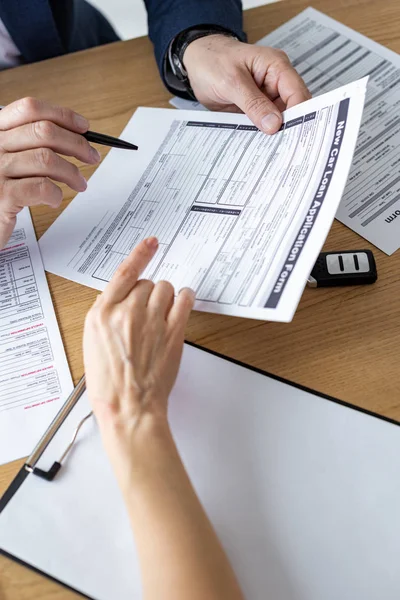 Cropped view of car dealer showing car loan application form to woman in office — Stock Photo