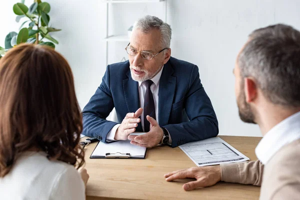 Selective focus of car dealer in glasses looking at customers while talking on office — Stock Photo