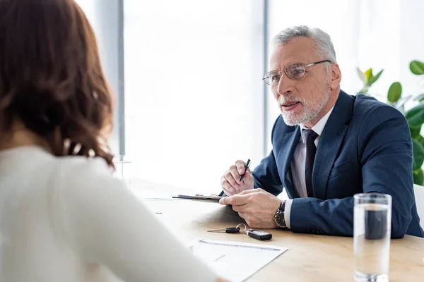 Autohändler mit Brille hält Klemmbrett neben Frau im Büro — Stockfoto