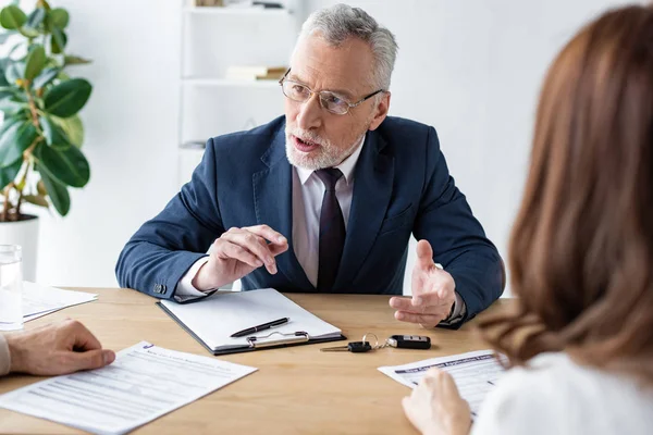 Selective focus of car dealer in glasses gesturing while talking with customers — Stock Photo