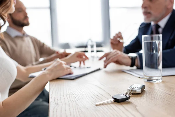 Selective focus of car keys near car dealer and customers — Stock Photo