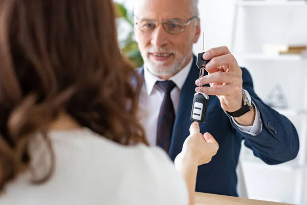 Selektiver Fokus des gut gelaunten Autohändlers, der Frau Autoschlüssel gibt — Stockfoto