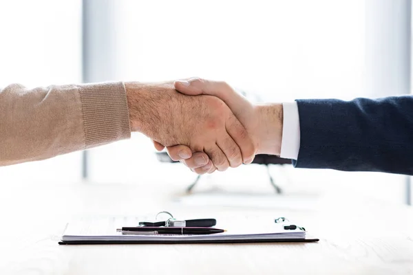 Cropped view of man and car dealer shaking hands in office — Stock Photo