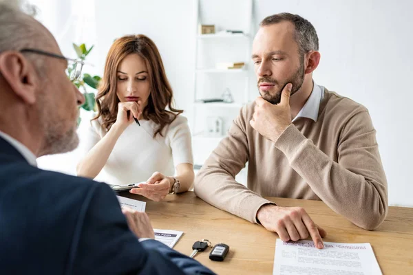 Selective focus of pensive man and woman sitting near car dealer in office — Stock Photo