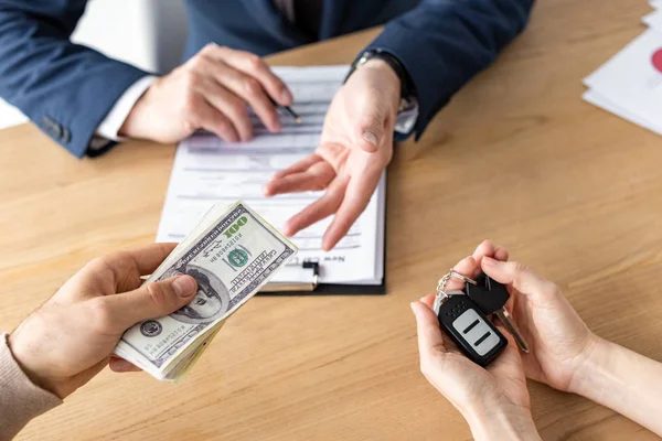 Vista recortada del hombre que da billetes de dólar al concesionario de automóviles cerca de la mujer que sostiene las llaves del coche - foto de stock