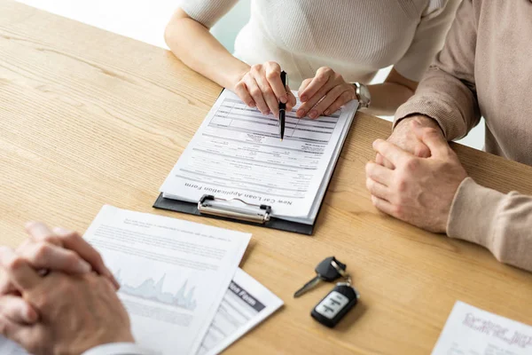 Cropped view of woman holding pen near clipboard while siting near men — Stock Photo