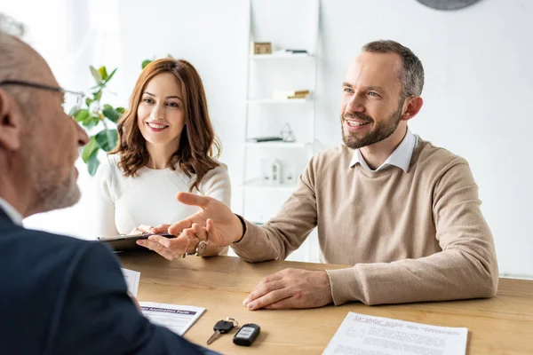 Happy man gesturing near woman with clipboard and car dealer — Stock Photo